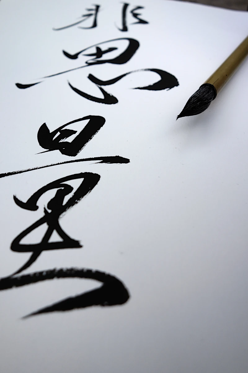 Un pinceau repose a cote d un texte calligraphie sur du papier blanc.